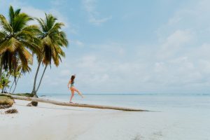 Una persona caminando sobre un tronco tumbado en una playa paradisíaca.